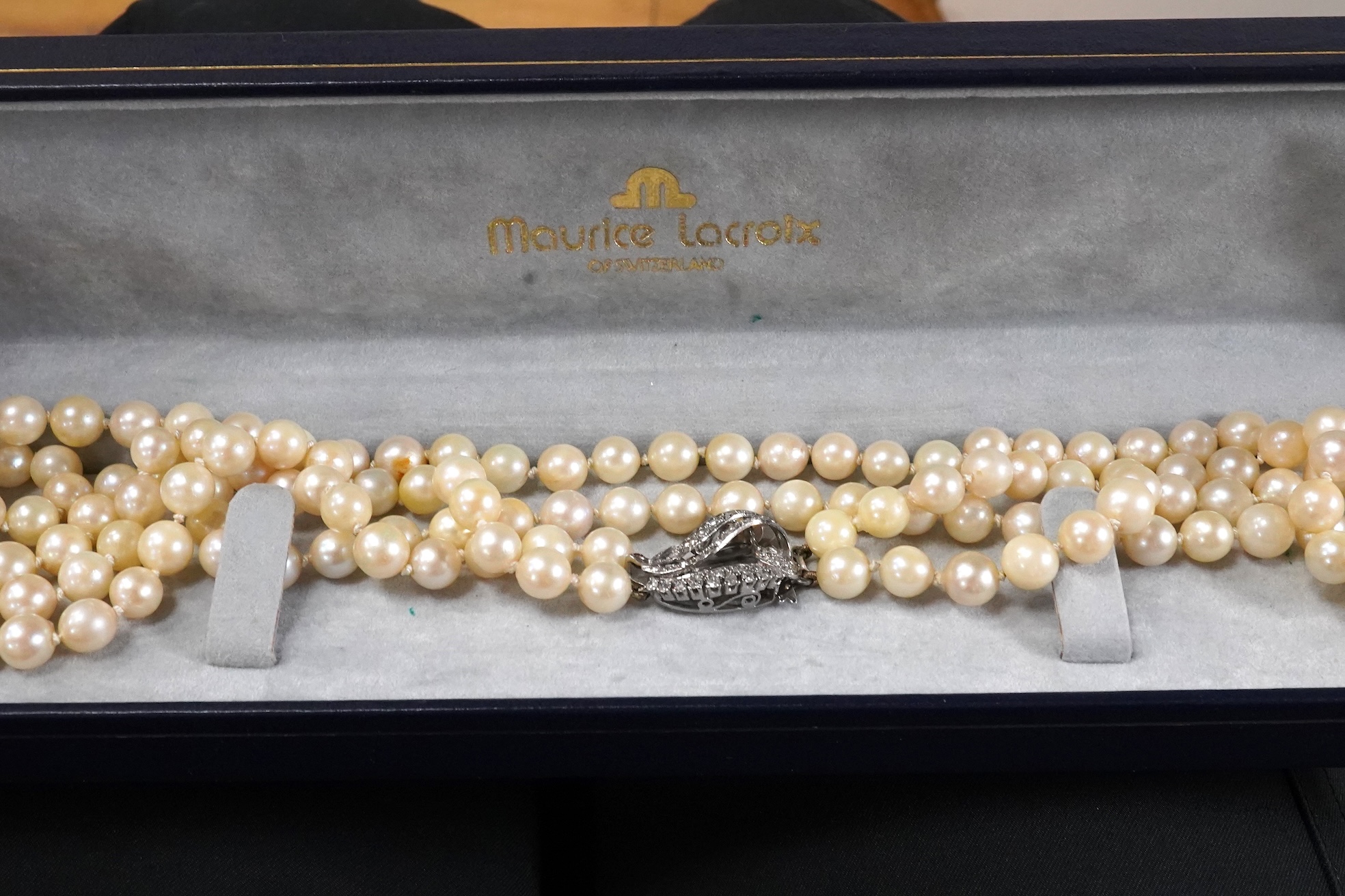A twin strand cultured pearl necklace with a diamond cluster set white metal scroll shaped clasp, 60cm.